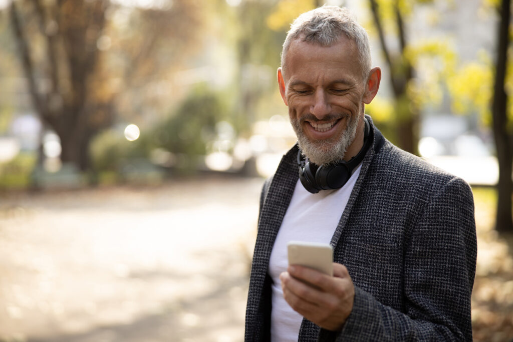 Cheerful handsome man standing outdoors and using smartphone